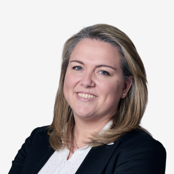 A woman with shoulder-length blonde hair, wearing a black blazer over a white shirt, smiles at the camera against a plain white background.