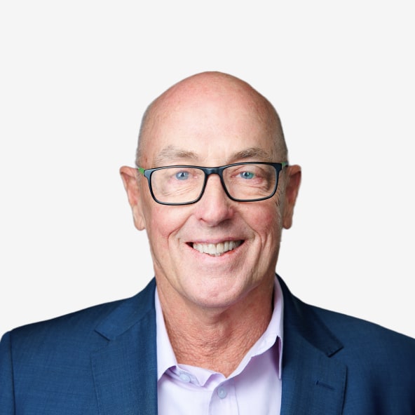 A smiling older man with glasses and a bald head, wearing a blue suit jacket and light purple shirt, posed against a plain white background.