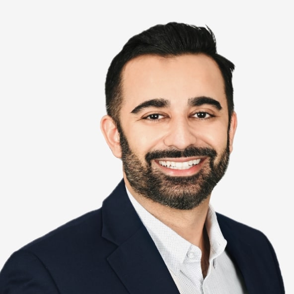 A man with dark hair and a beard, wearing a navy suit jacket and a light-colored shirt, smiles at the camera against a plain white background.