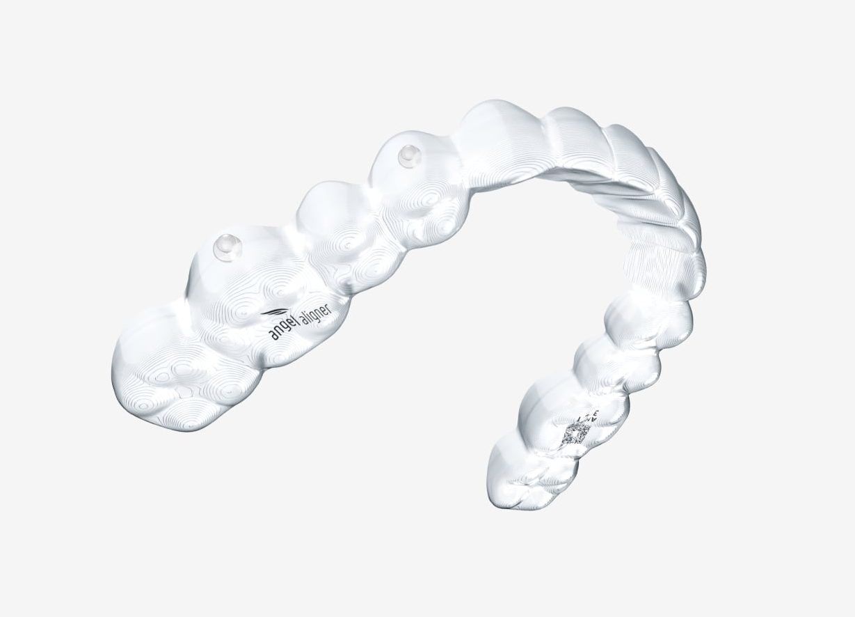 img-min A transparent dental aligner is shown on a plain white background, shaped to fit over a set of teeth, with subtle surface details and markings visible.
